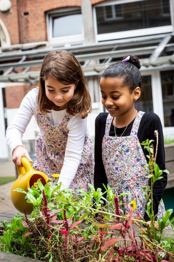 Twee meisjes geven planten water op de speelplaats van De Vlinders.